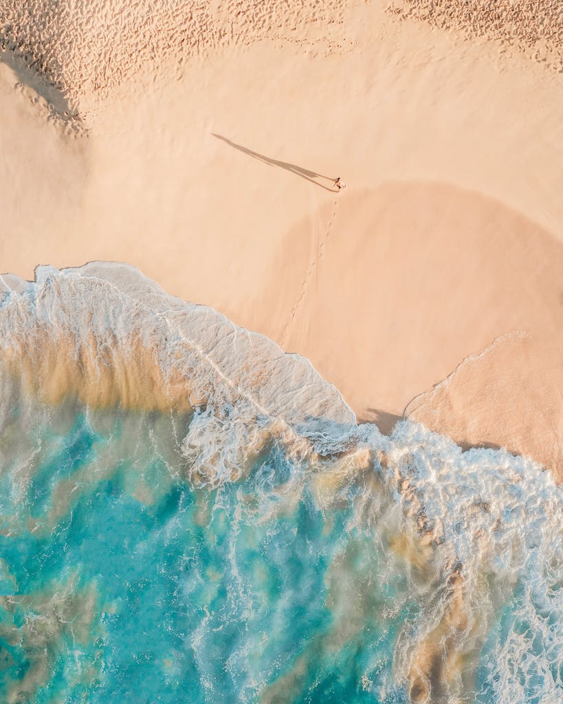 Drone view of anonymous person walking along sandy beach of turquoise sea in sunny day